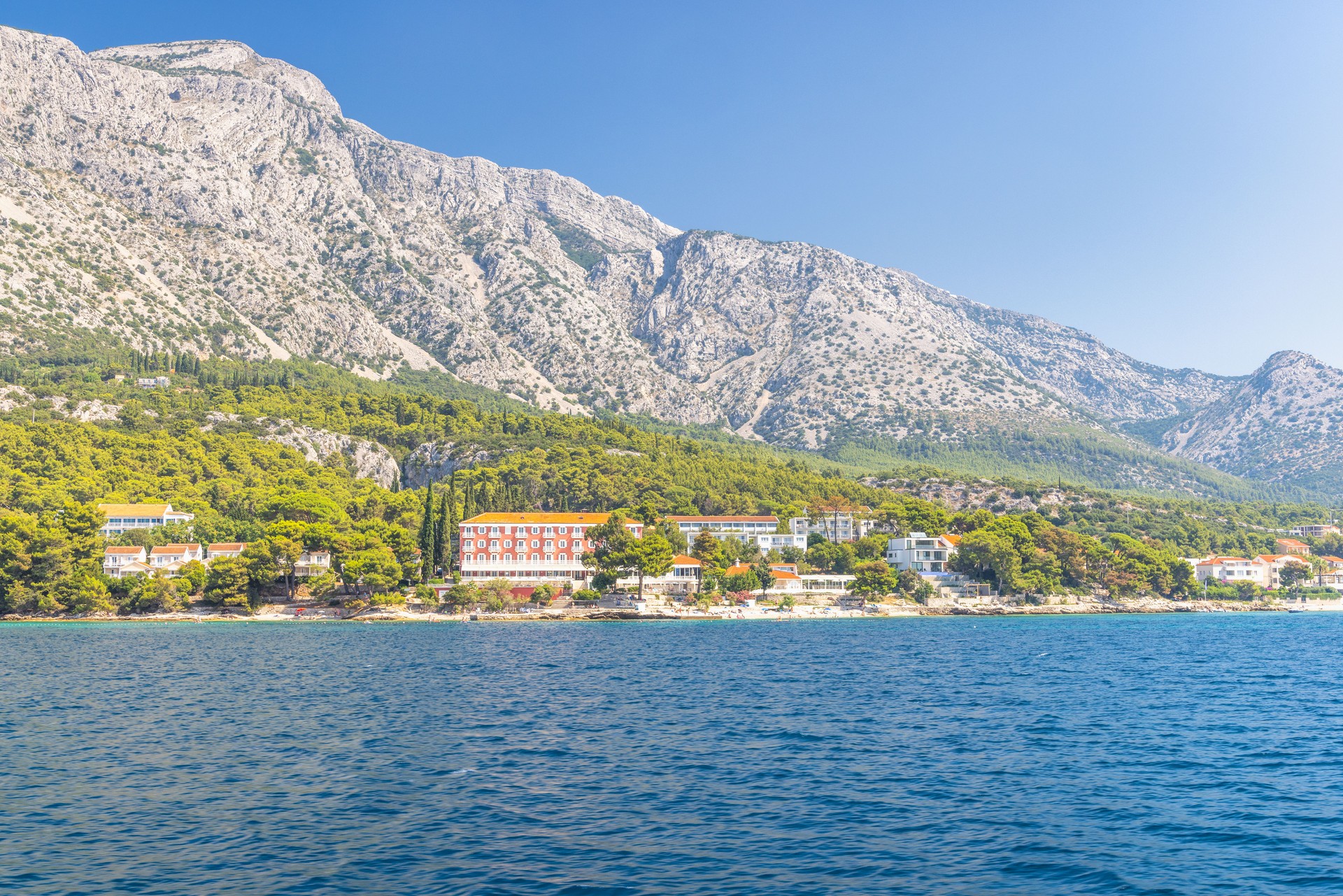 Sea coast of the Peljesac Peninsula in Croatia, Europe. Coastal view featuring mountains meeting the sea, green trees and buildings dotting the landscape on a clear, sunny day. Water is blue.